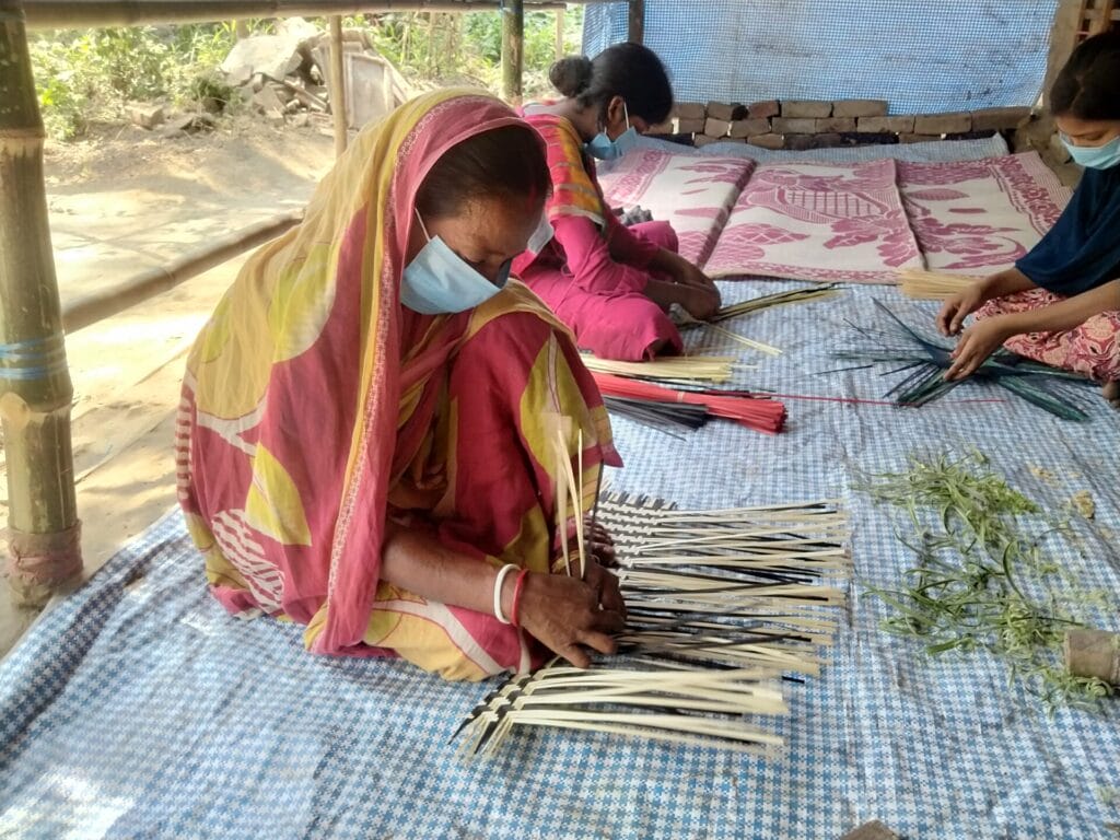 Women wearing masks weaving baskets outdoors
