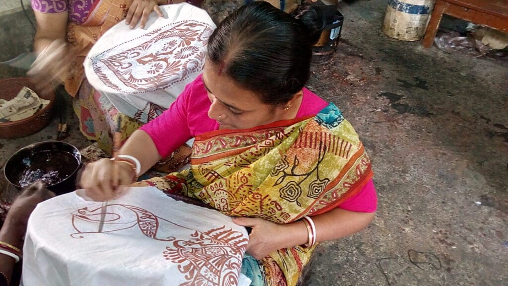 Woman painting traditional designs on white fabric