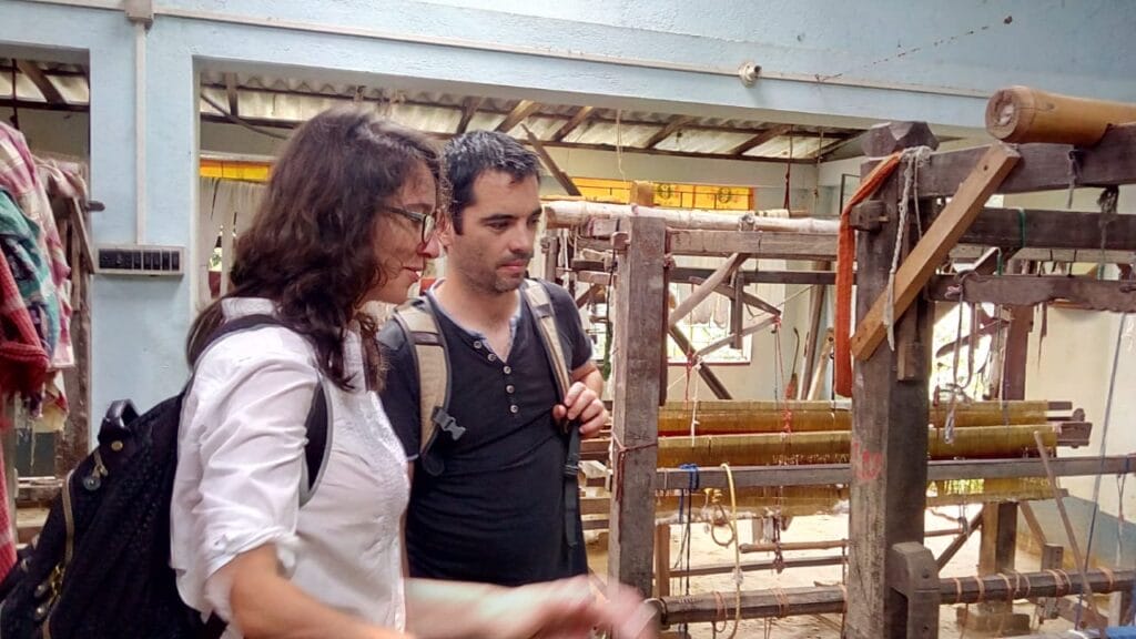 Two people examining wooden weaving loom indoors