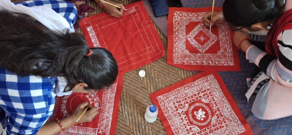 women artisans painting designs on red fabric