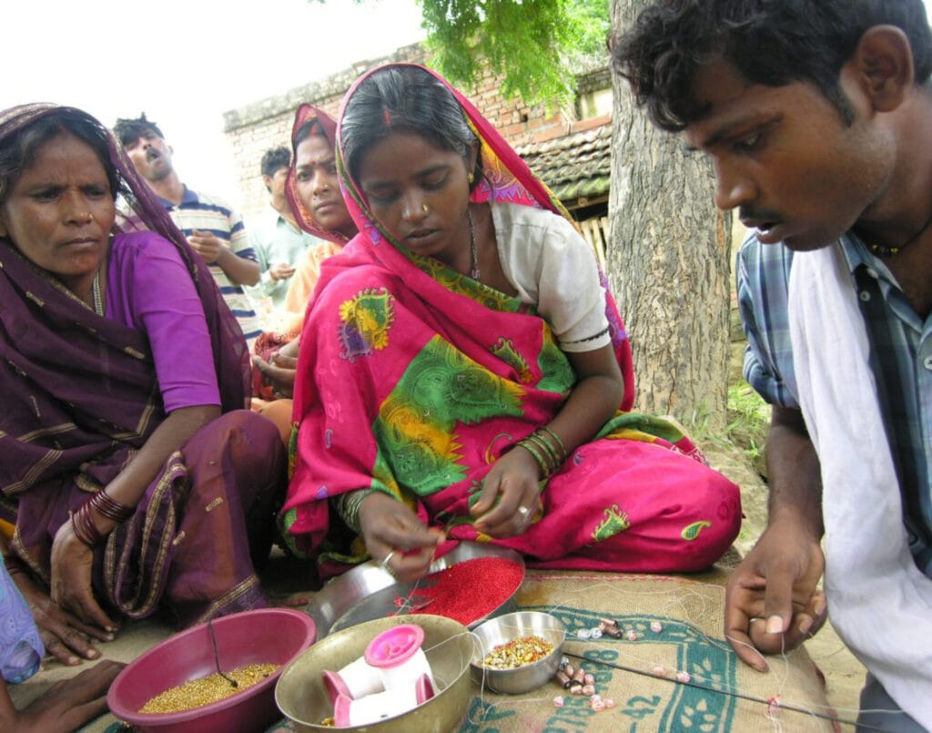 Women threading colorful beads outdoors together