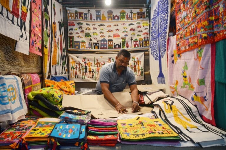Man arranging colorful embroidered textiles in market stall
