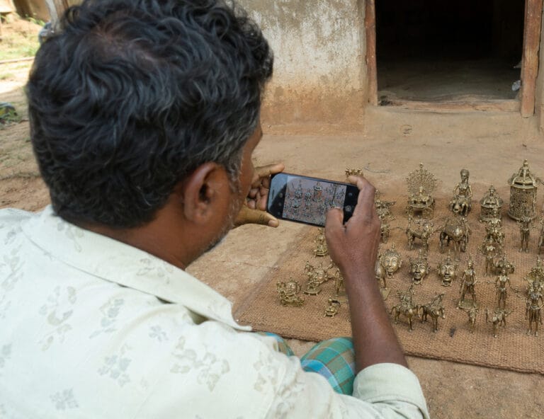 Man photographing brass figurines with smartphone outdoors